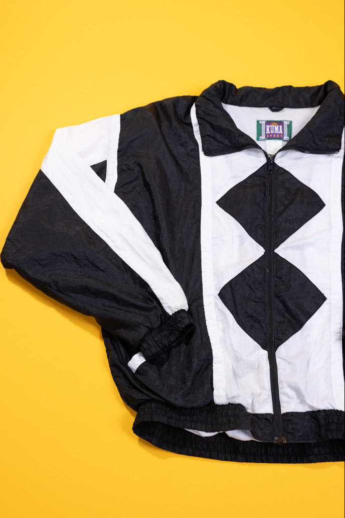 A black and white color-blocked windbreaker jacket with a diamond pattern on the front, laid flat on a bright yellow background.