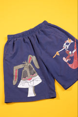 A pair of navy blue shorts featuring a large graphic of Bugs Bunny on the front and a smaller graphic of Looney Tunes characters on the side, displayed flat against a solid yellow background.